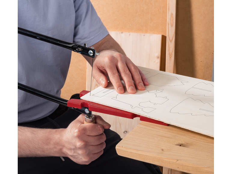 Man gebruikt een handzaag om ontwerpen uit een houten plank te zagen.