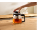 Hand plaatst deksel op glazen theepot met thee op een houten tafel.