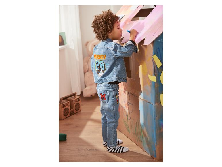 Een kind in een Mickey Mouse jeansjack en broek tekent op een kartonnen huis.