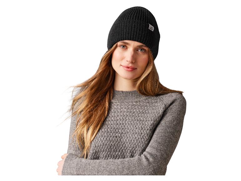 Een vrouw draagt een zwarte Sandqvist muts en een grijze trui.