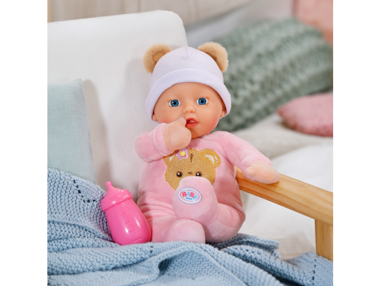 Zachte babypop in roze kruippakje en muts met berenoren naast een flesje.