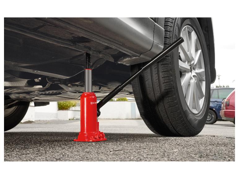 Rode hydraulische krik onder een grijze auto, die deze lichtjes van de grond tilt.