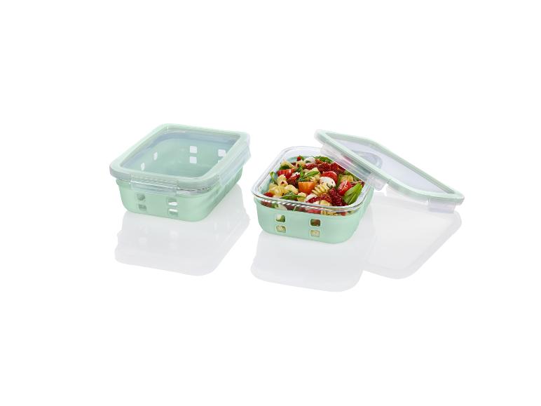 Twee groene glazen lunchboxen met deksel, één gevuld met pasta salade.