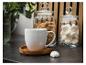Witte mok op een houten onderzetter met potten koekjes en meringues op de achtergrond.