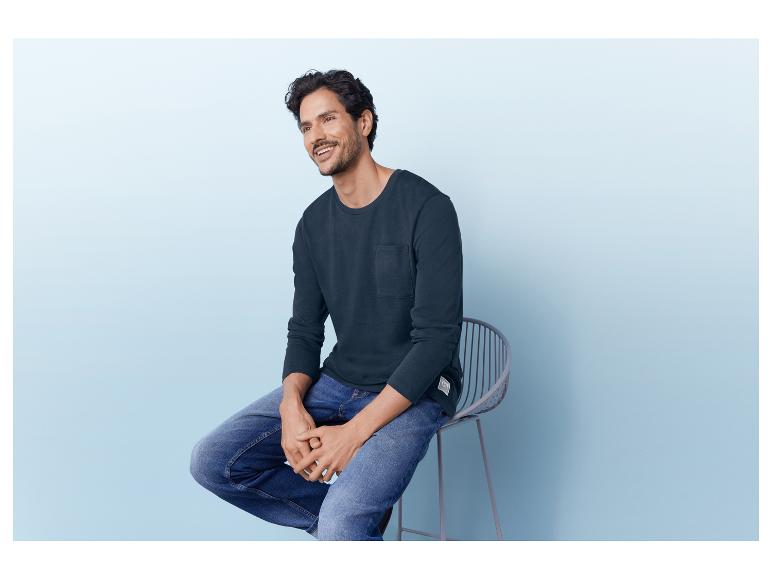 Man in een donkerblauwe longsleeve en blauwe jeans.