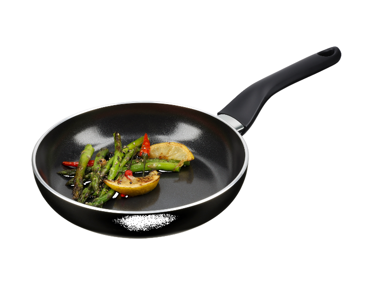 Een zwarte koekenpan met gebakken asperges, citroen en chili.