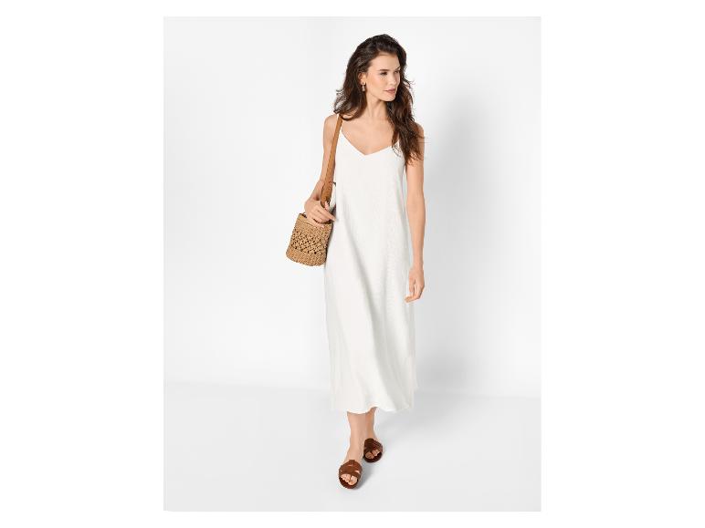 Vrouw in witte maxi-jurk, bruine sandalen en strooien tas.