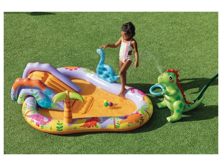 Opblaasbaar dinosauruszwembad met glijbaan en sproeier, met een klein meisje dat speelt.