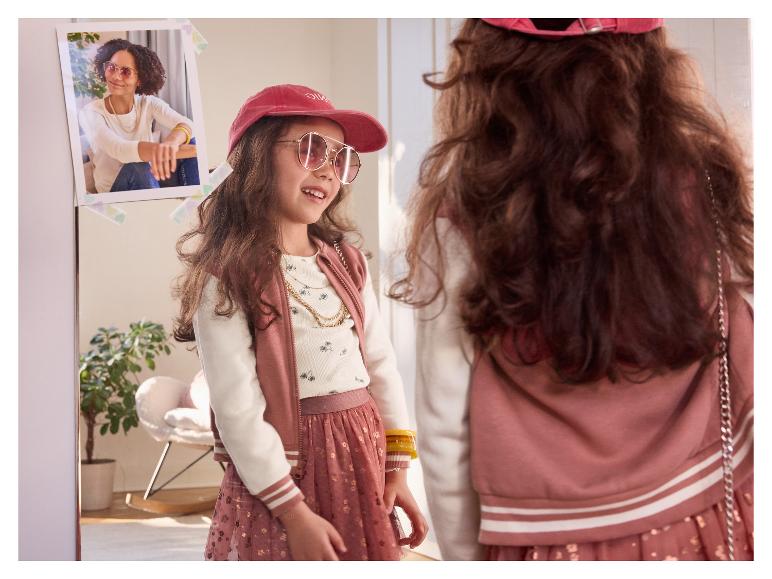 Meisje kijkt in de spiegel met pet en zonnebril.