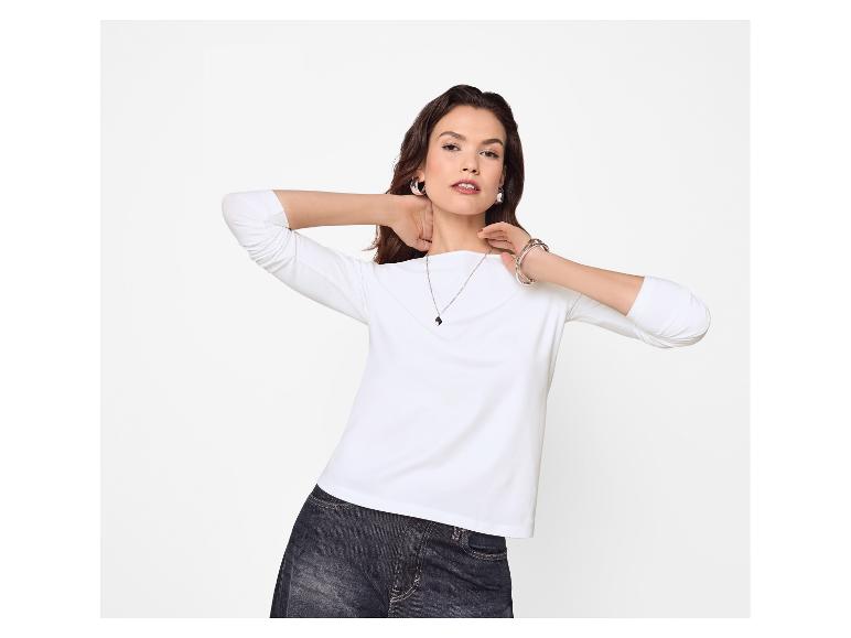 Vrouw in een wit shirt met lange mouwen en donkere jeans, met sieraden.