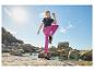 Vrouw in zwart T-shirt en fuchsia legging sportend op rotsachtig strand.