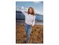 Vrouw in witte trui en jeans op het strand, lachend, met de zee op de achtergrond.