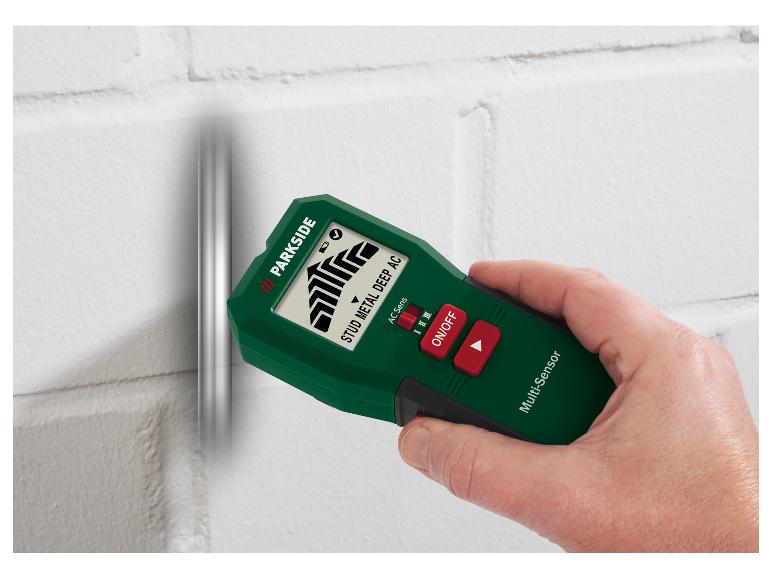 Groene en zwarte multifunctionele wanddetector, vastgehouden door een hand, op een witte muur.