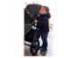Peuter in donkerblauwe jas en jeans staat naast een kinderwagen.