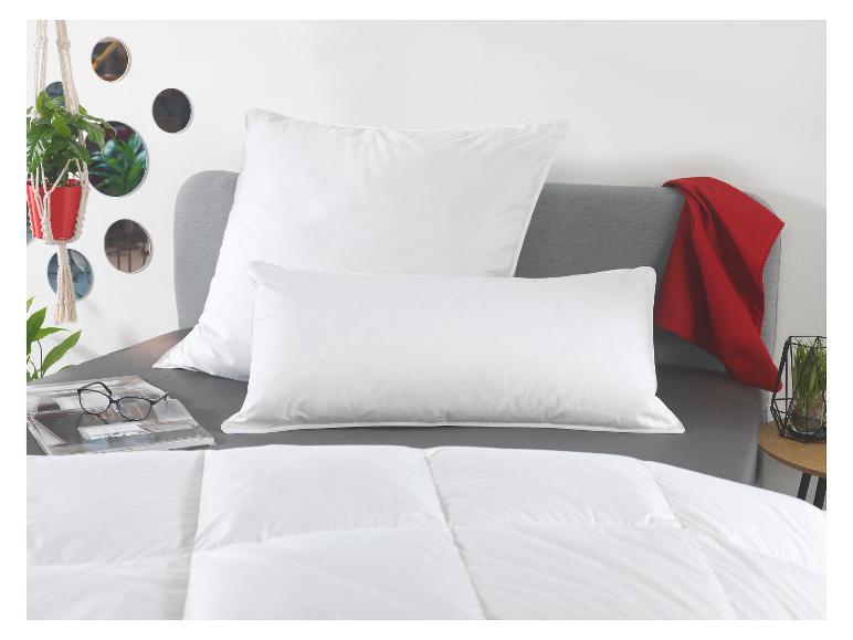 Wit dekbed en kussens op een bed met grijs beddengoed en een rode plaid.