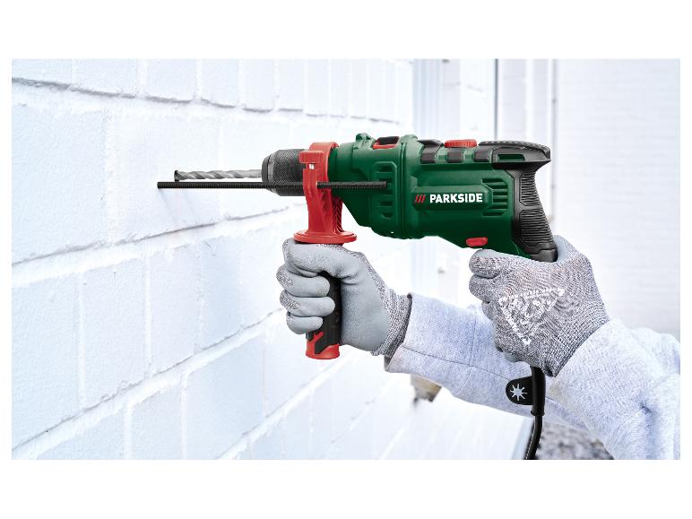 Man in beschermende handschoenen boort in een witte muur met een klopboormachine.