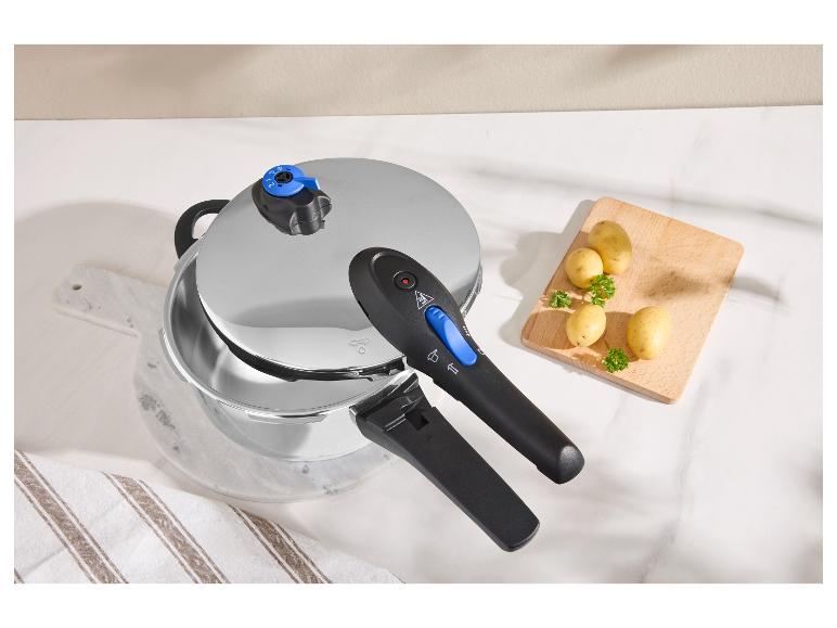Metalen snelkookpan met zwarte handvatten en aardappelen op een marmeren tafel.