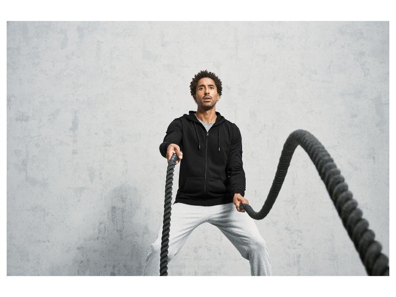 Man in een zwarte hoodie en grijze trainingsbroek werkt met een zware touw tijdens een work-out.