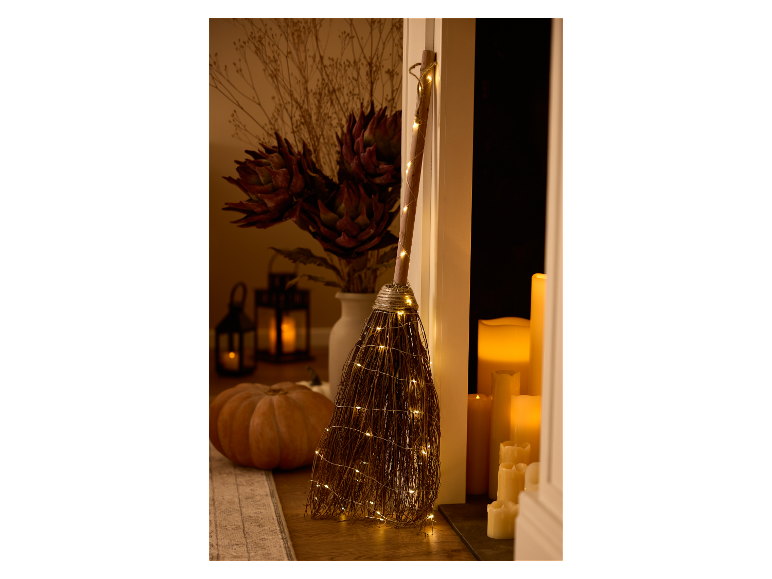 Verlichte Halloween heksenbezem met pompoen en lantaarns.