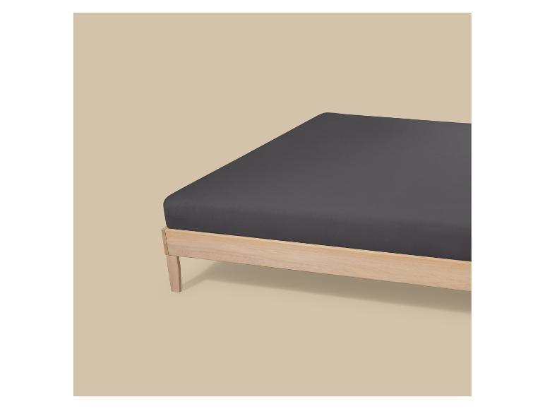 Bed met houten frame en donkergrijs hoeslaken op een beige achtergrond.