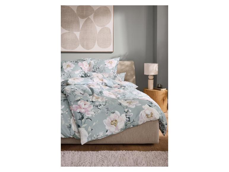 Bed met lichtblauw bloemendekbed en kussens, met een lamp en boeken op een houten nachtkastje.