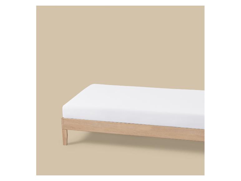 Een wit matras op een licht houten bedframe tegen een beige achtergrond.