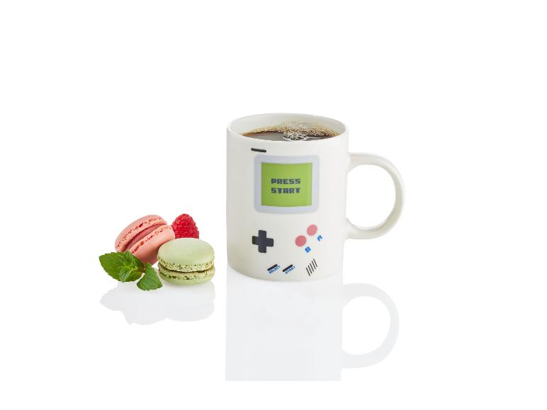Een mok met een retro game ontwerp, gevuld met koffie en macarons.