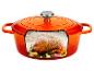 Oranje gietijzeren braadpan met een gebraden kip, knoflook en kruiden erin.