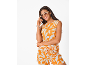Lachende vrouw in oranje top en korte broek met witte bloemenprint, zonnebril en creolen.