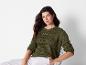 Een vrouw draagt ​​een groene trui met opengewerkte details en witte broek.