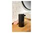 Een zwarte automatische zeepdispenser op een houten aanrecht in een badkamer.