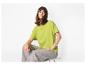 Vrouw in een limoengroen T-shirt en grijze jeans, zittend op een kruk.