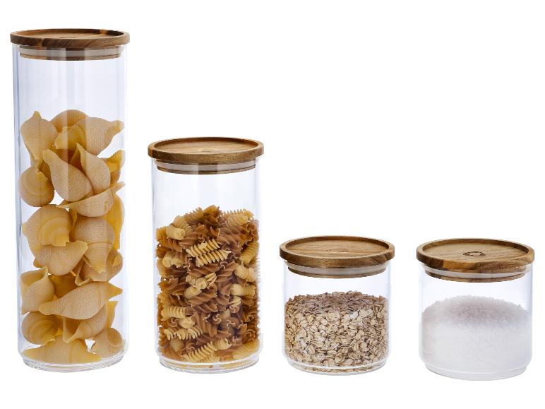 Vier glazen potten met houten deksels, gevuld met pasta, haver en zout.