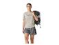 Vrouw in een beige T-shirt met bergprint en grijze shorts, met een zwarte rugzak op haar schouder.