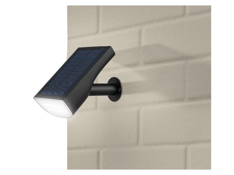 Zwarte LED-zonnelamp met zonnepaneel, gemonteerd op een beige bakstenen muur.