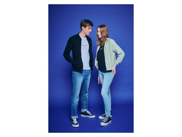 Twee jonge mensen dragen jassen en jeans tegen een blauwe achtergrond.