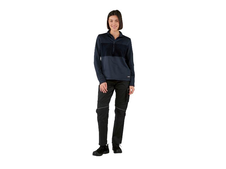 Vrouw in donkerblauwe sweater en zwarte werkbroek met reflectoren.