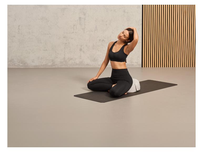 Een vrouw zit op een yogamat met een kussen voor ondersteuning.