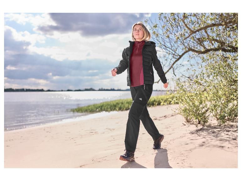Vrouw in een bordeauxrood CRIVIT functioneel shirt wandelt op een zandstrand.