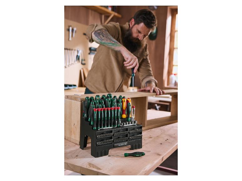 Een man gebruikt een schroevendraaier uit een grote set schroevendraaiers en bits op een houten werkbank.