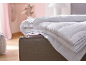 Gevouwen wit dekbed met blauwe bies op een bed in een slaapkamer met roze muren.