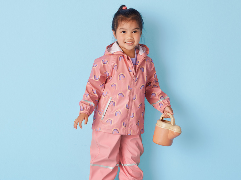 Een meisje draagt een regenjas met regenboogprint en houdt een gieter vast.