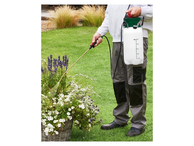 Persoon besproeit planten in een tuin met een schoudergedragen drukspuit.