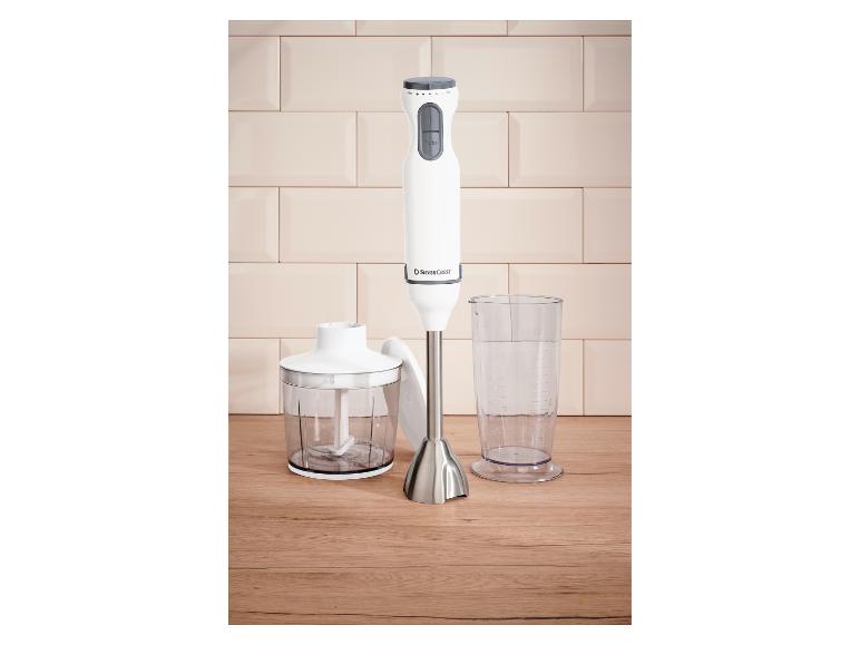 Witte staafmixer met hakmolenopzetstuk en maatbeker op een houten ondergrond.