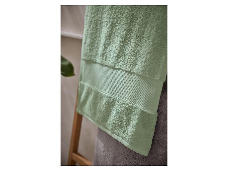 Lichtgroene handdoek met een gestructureerde band, hangend aan een houten ladder in een badkamer.