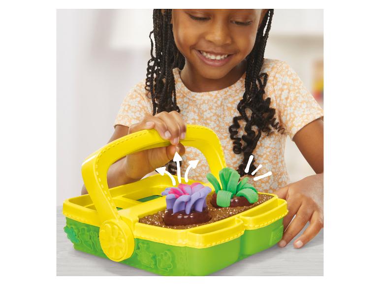 Lachend kind speelt met een Play-Doh tuiniermandje met kleibloemen en -groenten.