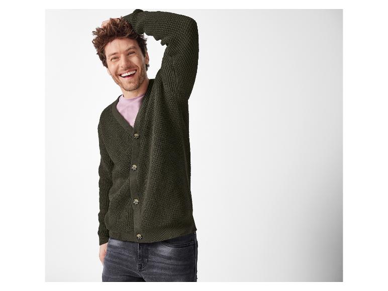 Een lachende man in een donkergroen vest en donkere jeans.