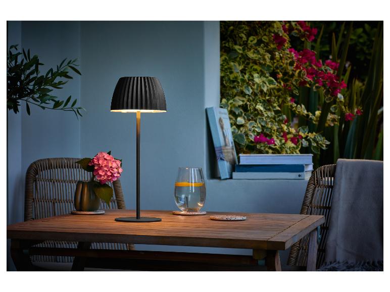Tafellamp op een houten tafel met bloemen en een drankje op een terras.