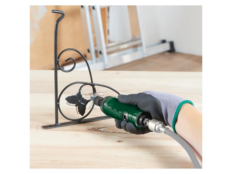Gehandschoende hand gebruikt groen roterend gereedschap om een zwarte metalen beugel te schuren.