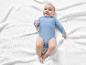 Een baby in een blauwe romper op een witte deken.